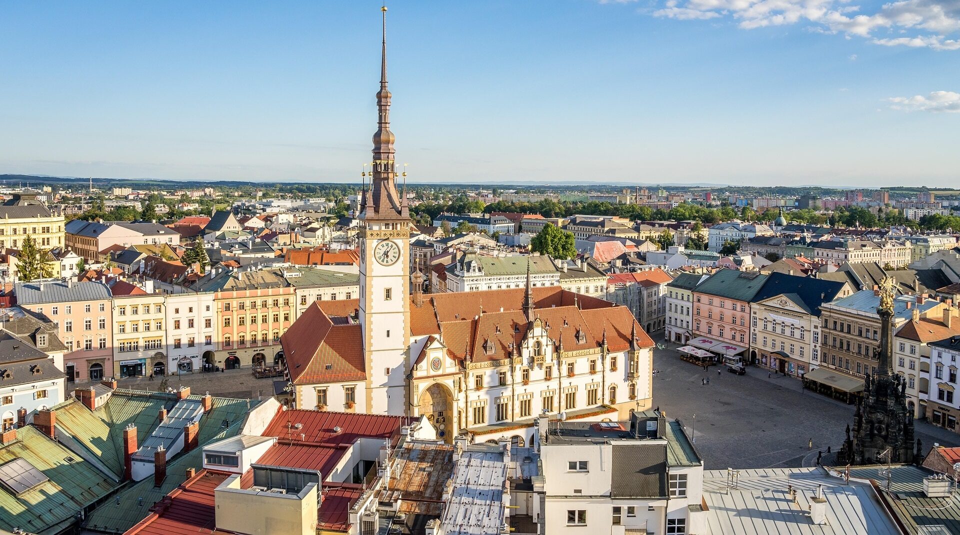Aerial view of a European town square with a tall clock tower and red-tiled rooftops under a clear blue sky?re full daylight atmosphere.