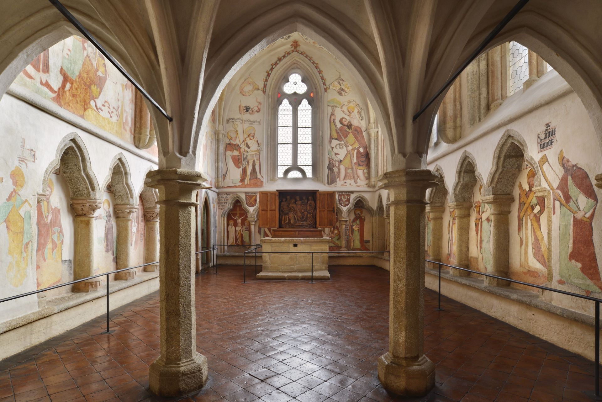 Interior of a medieval church with stone arches, painted walls, and a central altar under a gothic window
