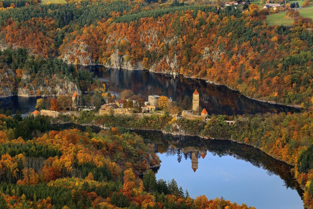 Aerial view of a medieval fortress on a river bend surrounded by autumn-colored trees in orange, yellow, and green (fall foliage).