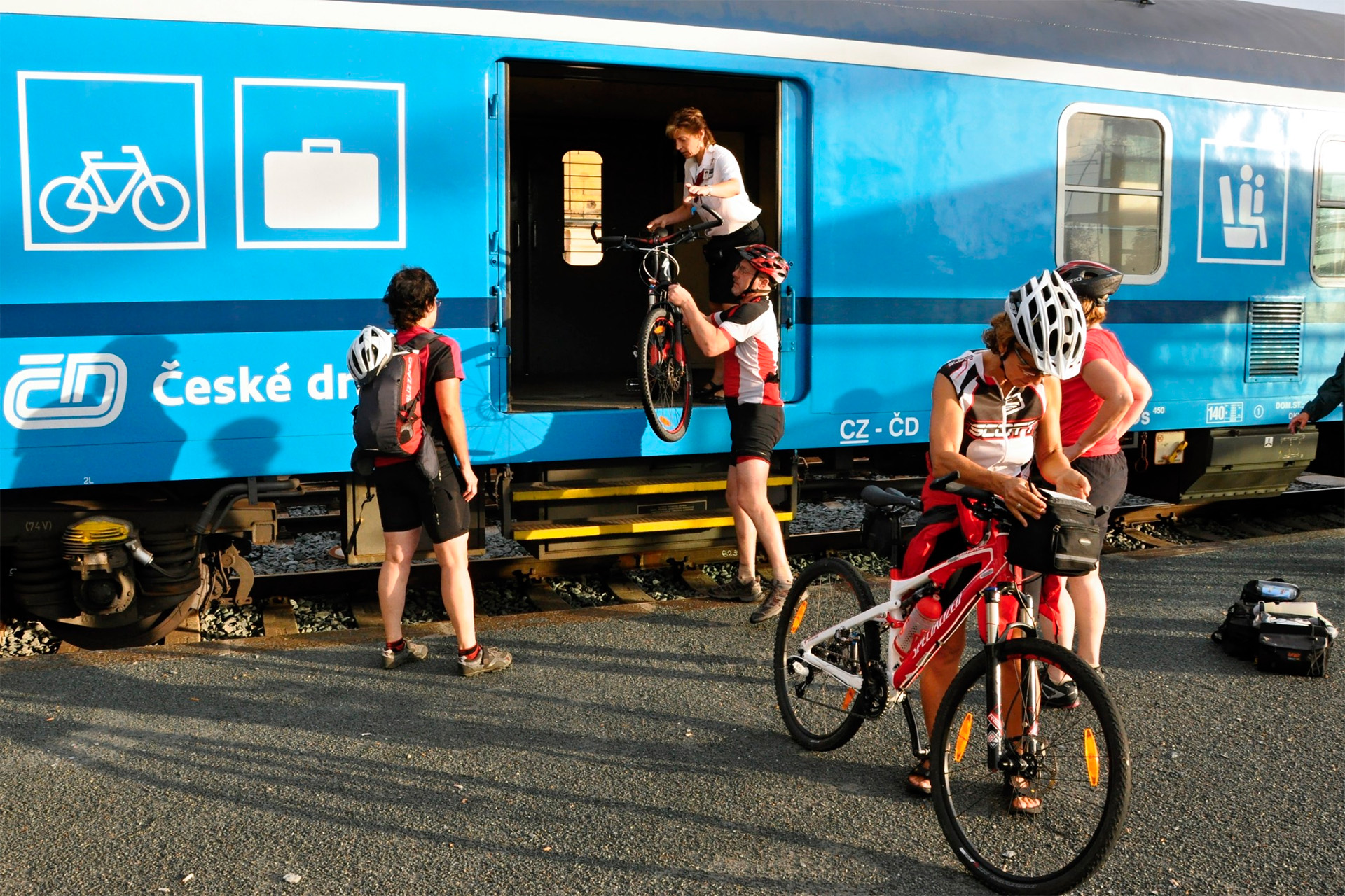 Pessoas com capacetes de ciclismo guardando apetrechos em vagão de trem especial para bikes.